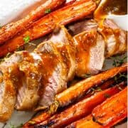 sliced pork tenderloin and whole carrots on a serving platter with gravy poured on sliced meat.