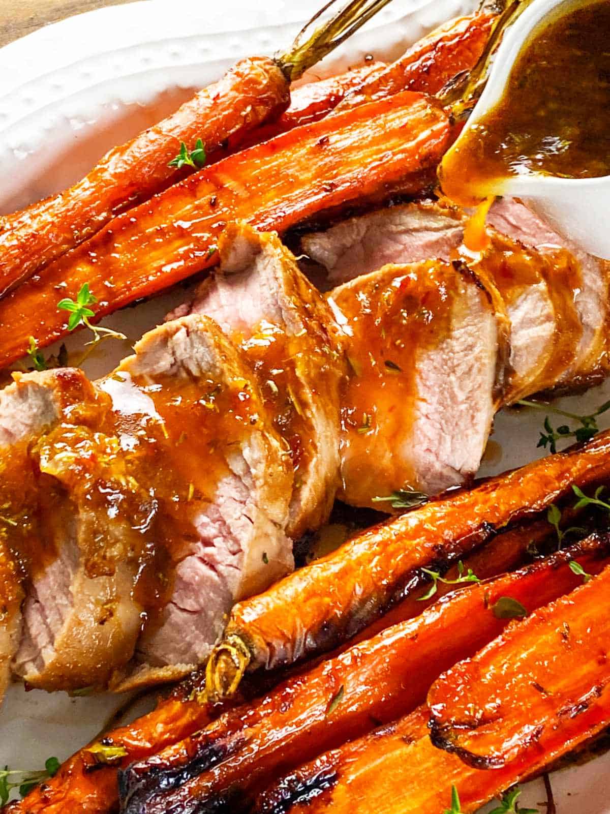 sliced pork tenderloin and whole carrots on a serving platter with gravy poured on sliced meat.