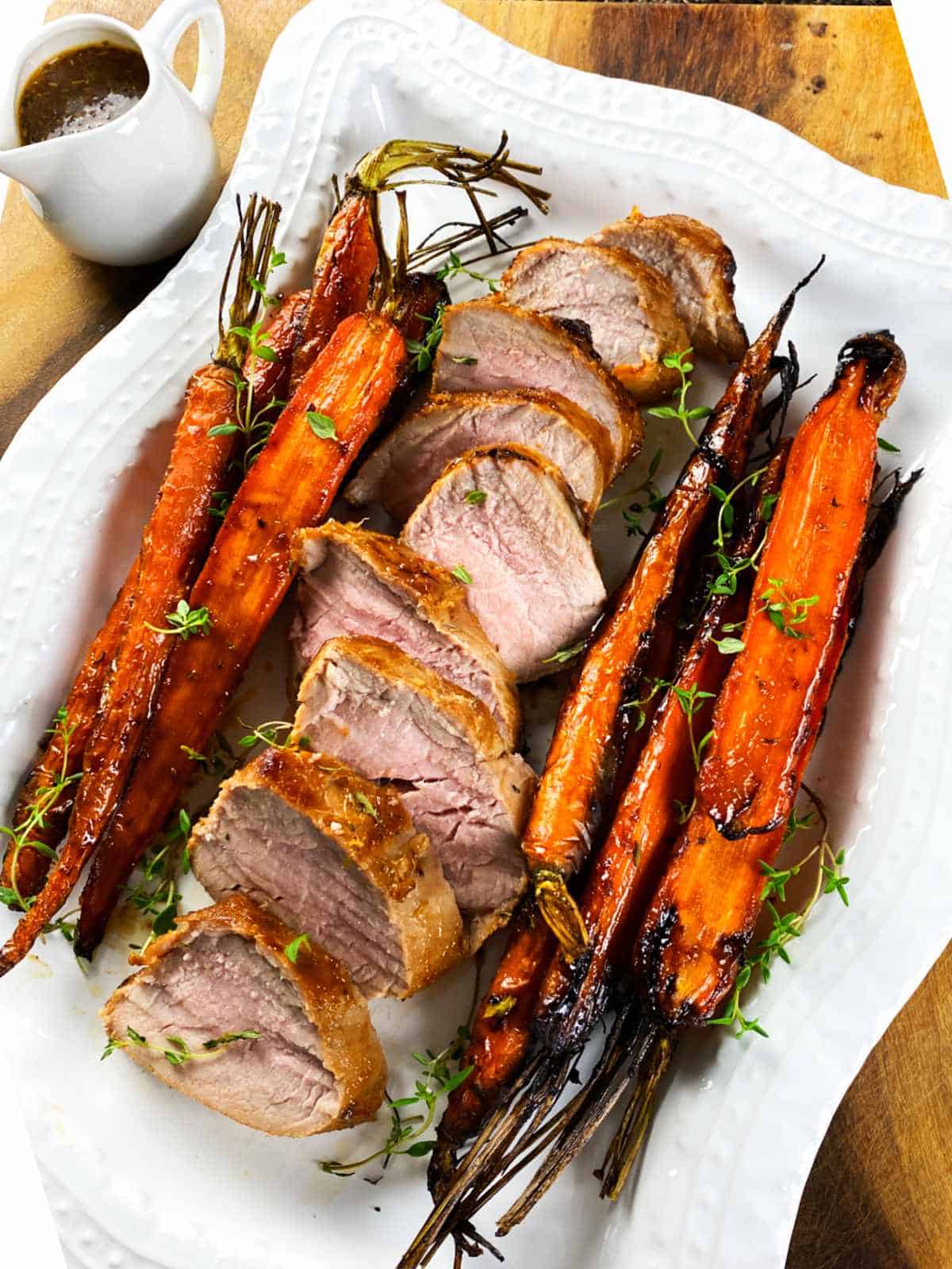 sliced pork tenderloin and whole carrots on a serving platter.