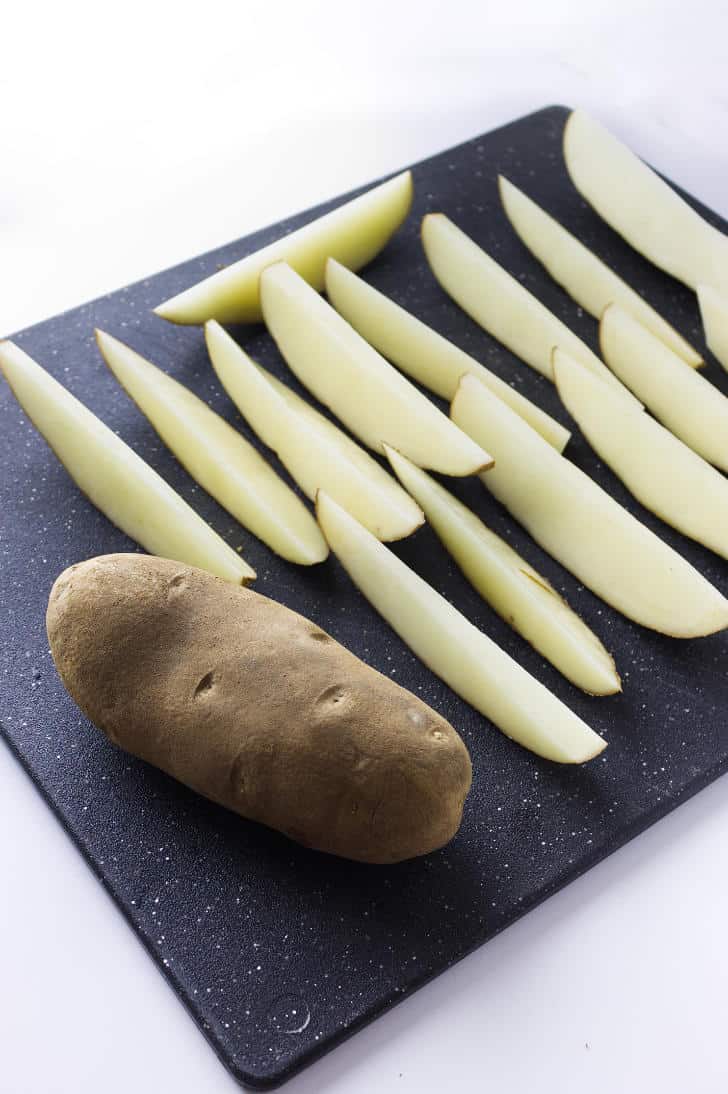 black cutting board with russet potatos cut into long wedges.
