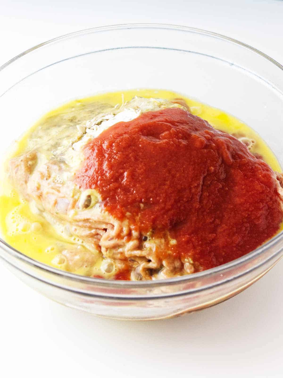 egg and tomato sauce added to ground turkey in bowl.