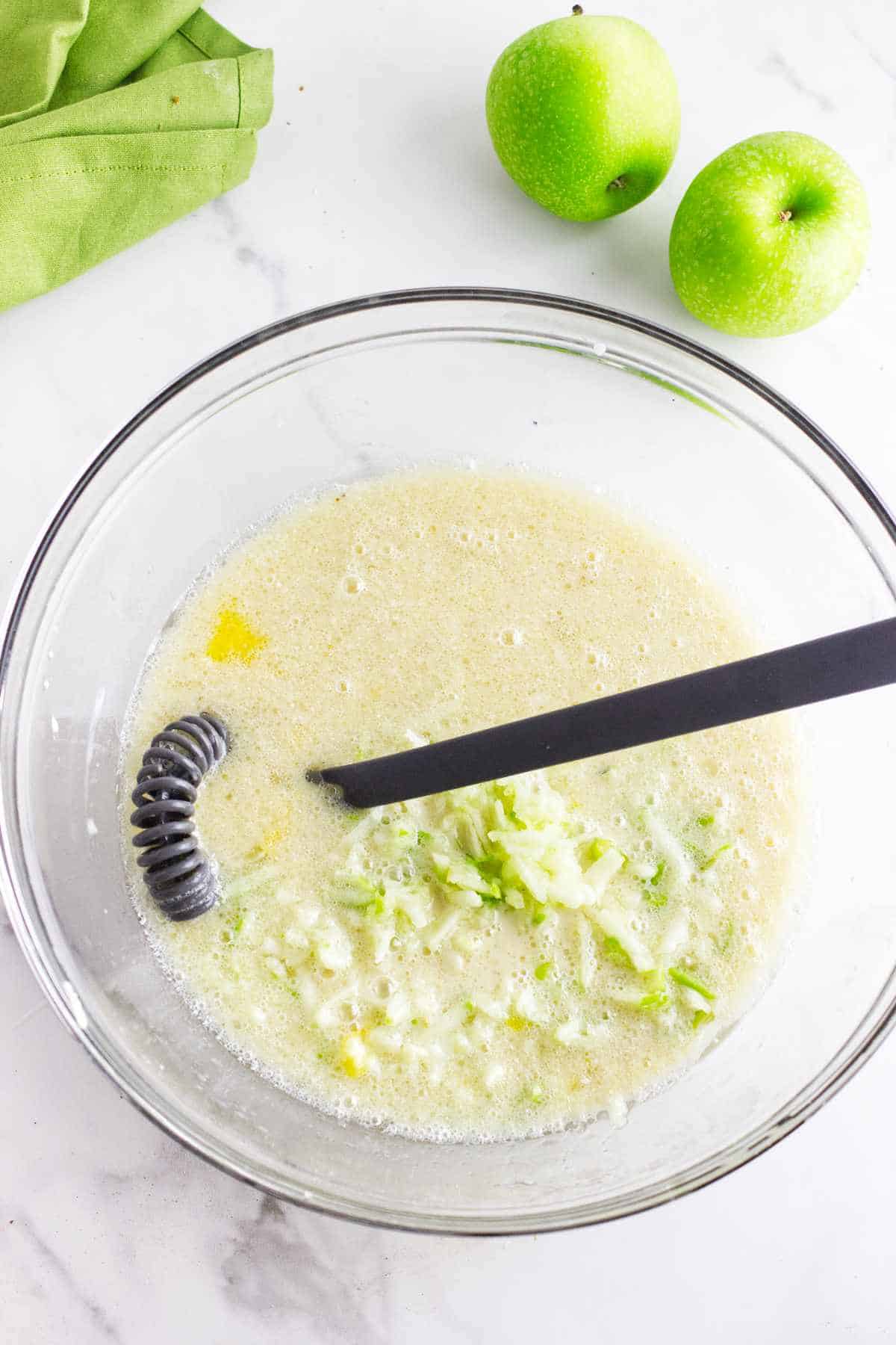 vegetable oil and grated apples mixed into liquid in a bowl.