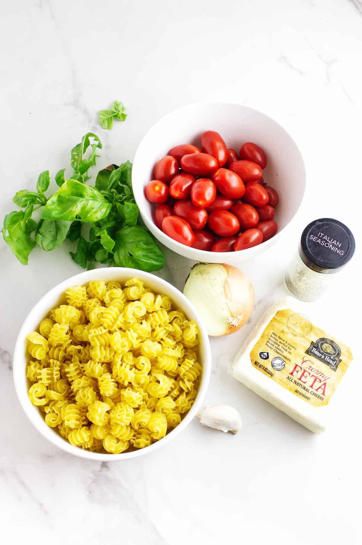 pasta, feta, seasonings, and grape tomatoes on a white background.