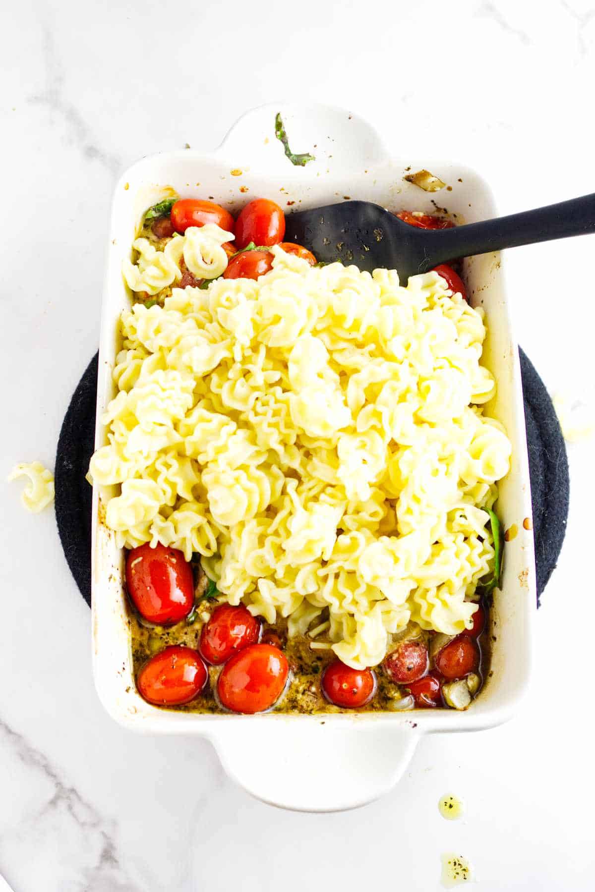 cooked pasta added to baking dish with cooked cherry tomatoes and cheese.
