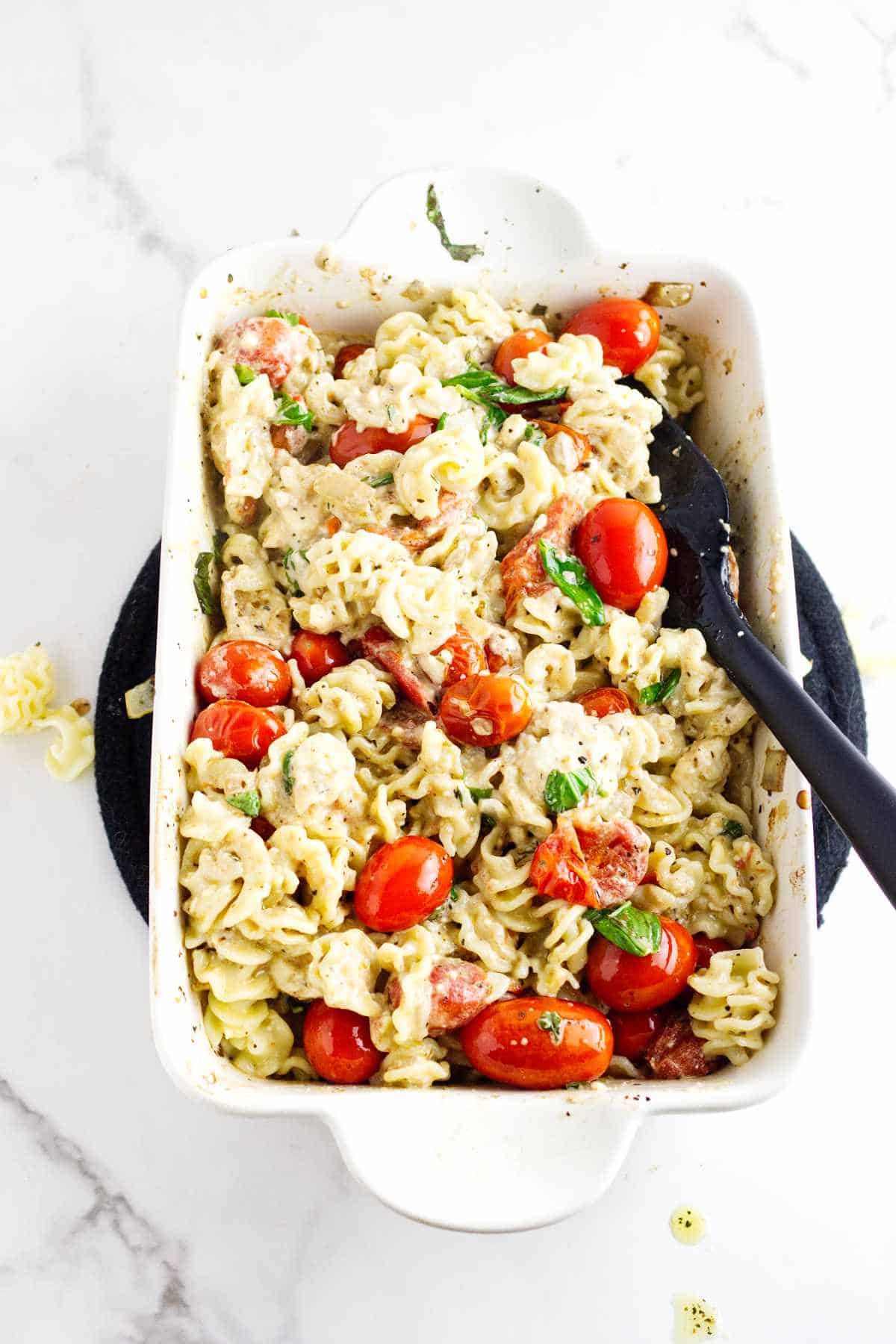 cooked pasta mixed into cooked cherry tomatoes and cheese in a baking dish.