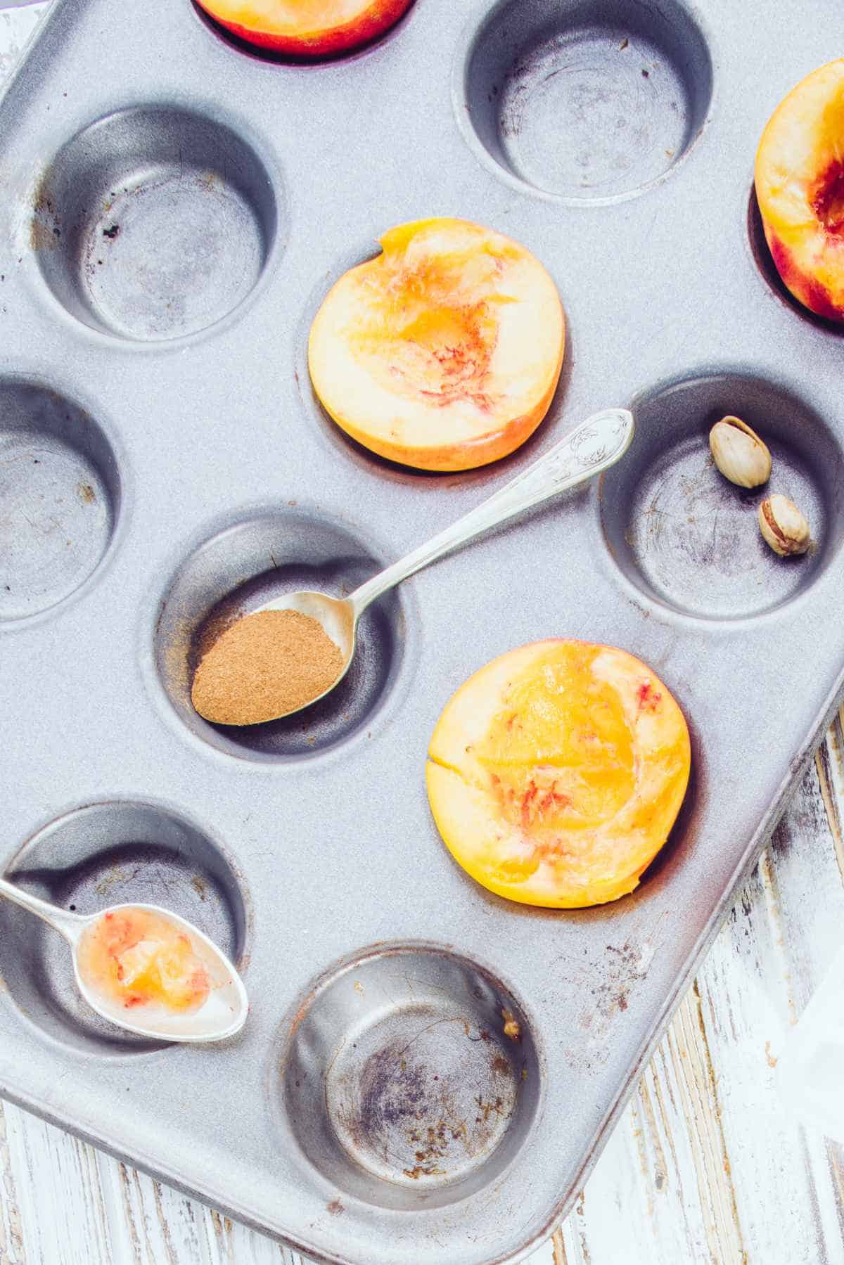 halves of stone fruit in a muffin tin with honey and cinnamon.