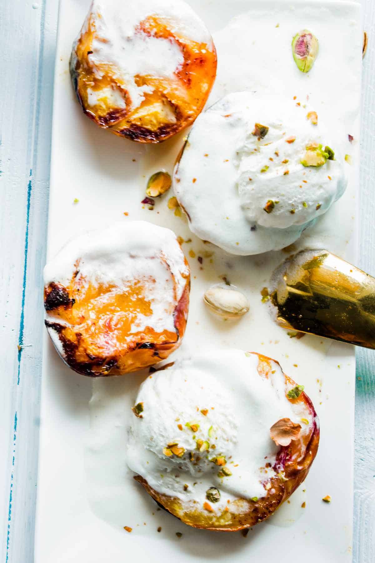 baked peaches on a platter with ice cream and chopped pistachio nuts.