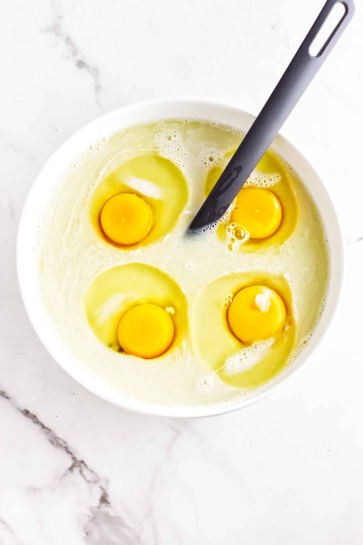 bowl of eggs, milk, and cream with a whisk.