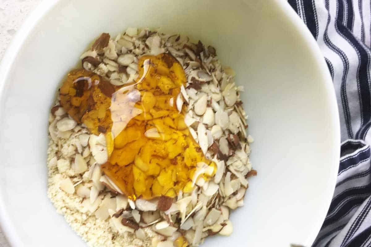 almonds, honey, flour, salt, and oats added to a bowl.