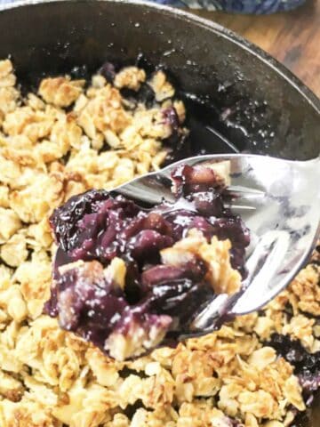 close up of a spoonful of blueberry crisp from a cast iron skillet.
