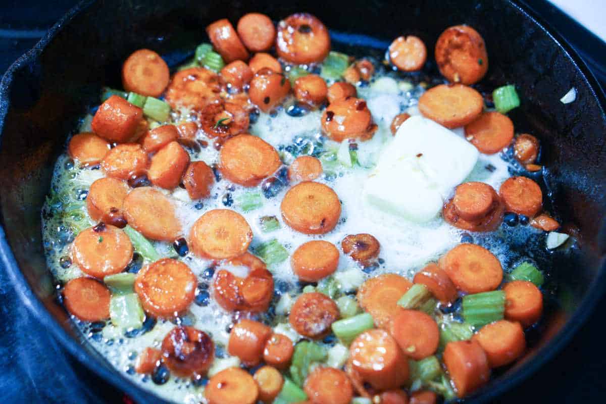 carrots, onions, and celery sauteing in some butter in a skillet.