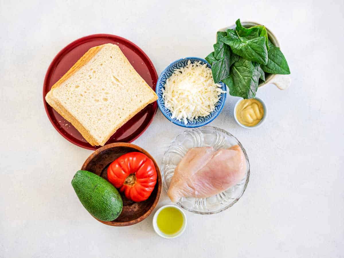 avocado, chicken, tomato, mozzarella, spinach, and sandwich bread ingredients on a white background.