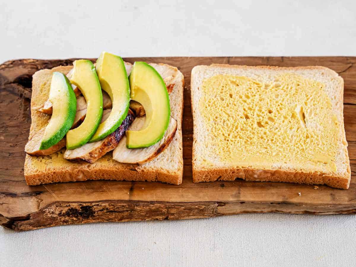 avocado, chicken, and mustard on white bread slices.