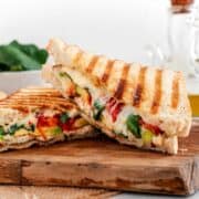 Diagonally sliced grilled chicken avocado panini on a cutting board.