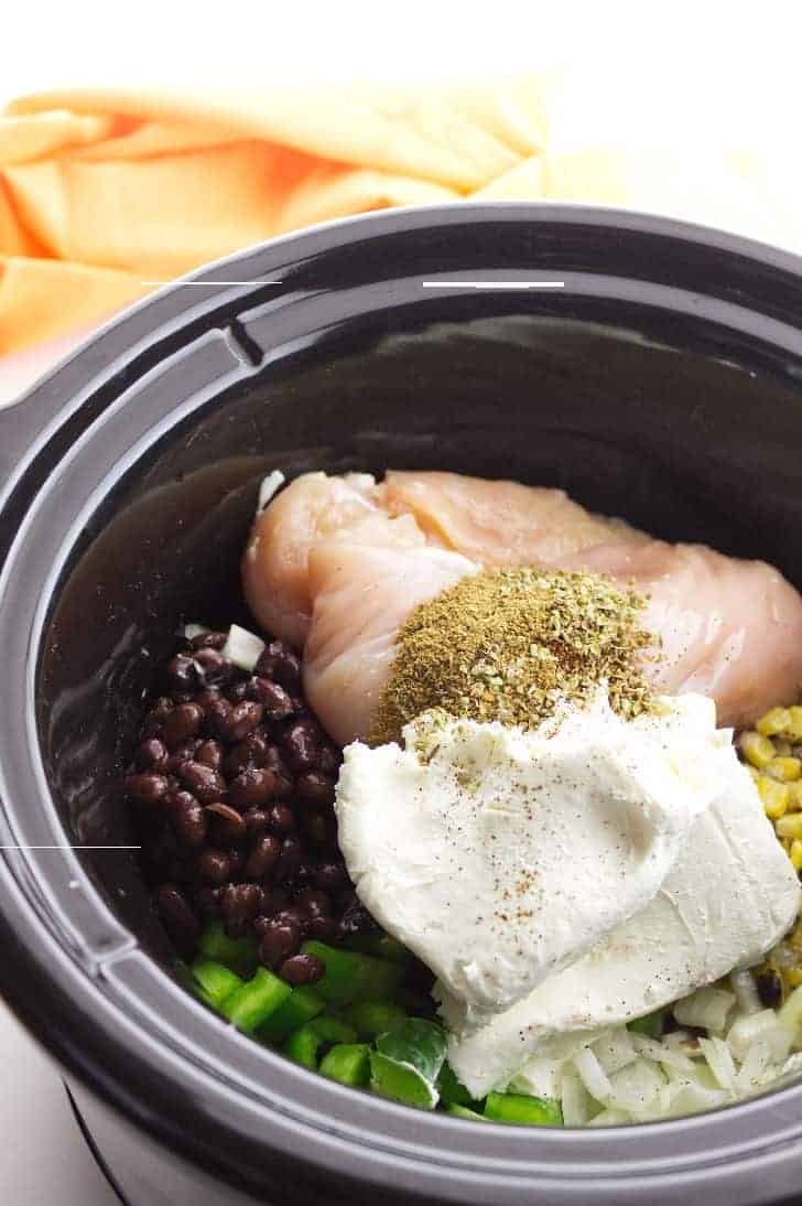 ceramic crockpot bowl with chicken, black beans, corn, and chopped vegetable.