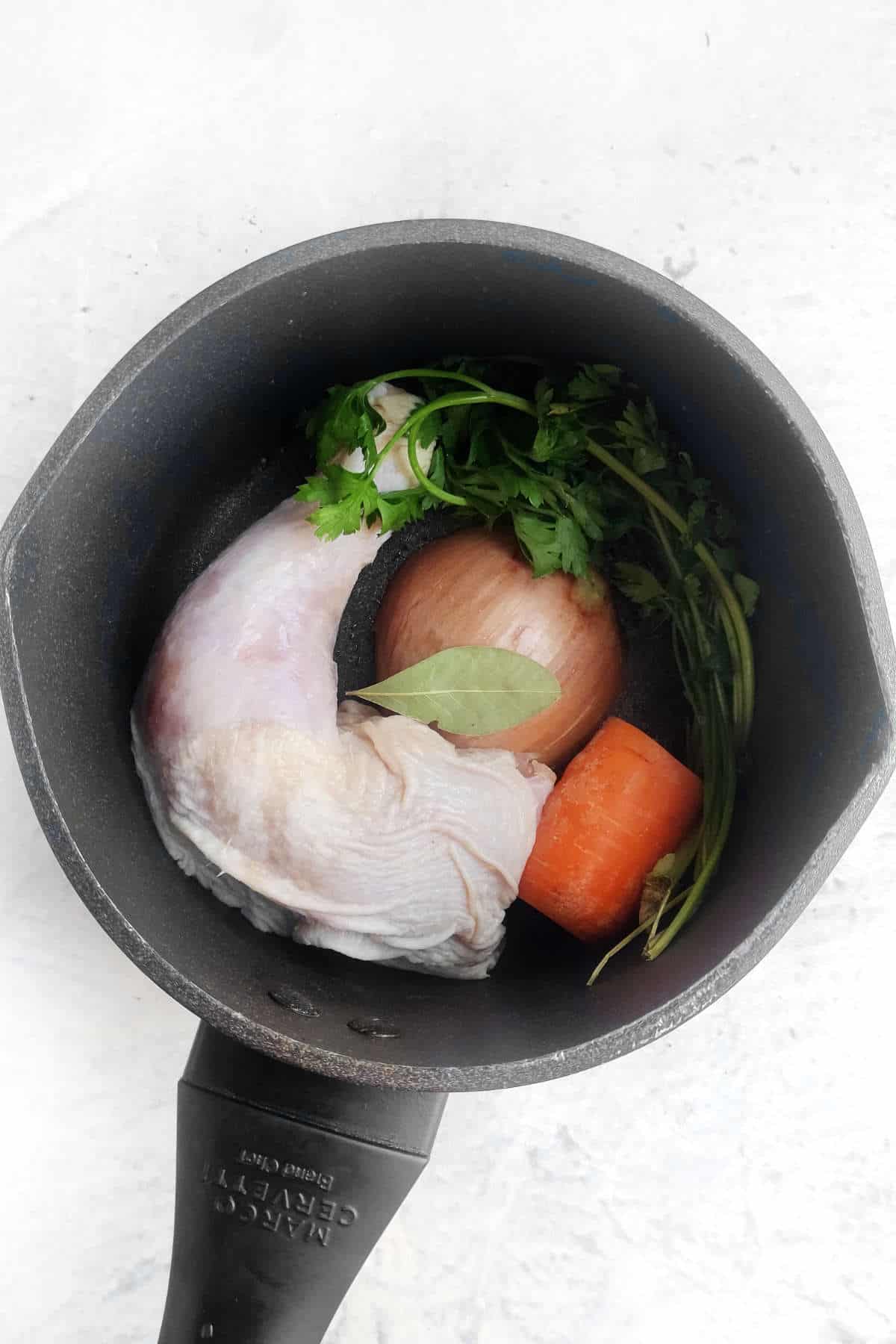sauce pan with chicken, herbs, carrot, and onion simmering in water.