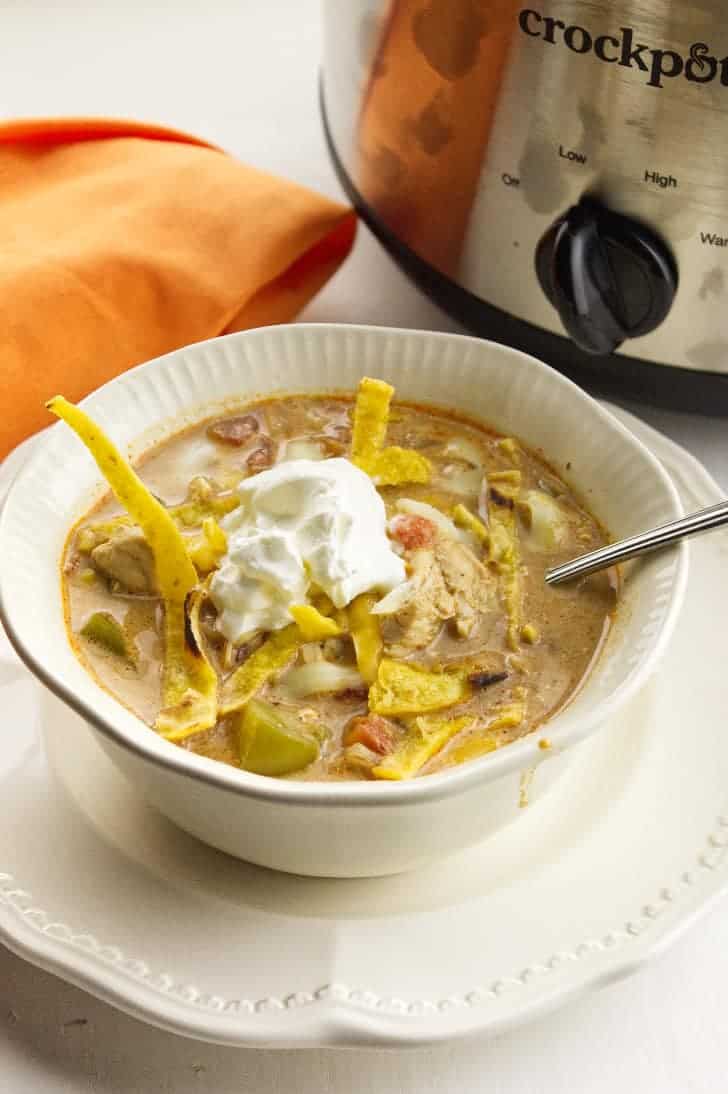 white bowl serving chicken enchilada soup, with crockpot in background