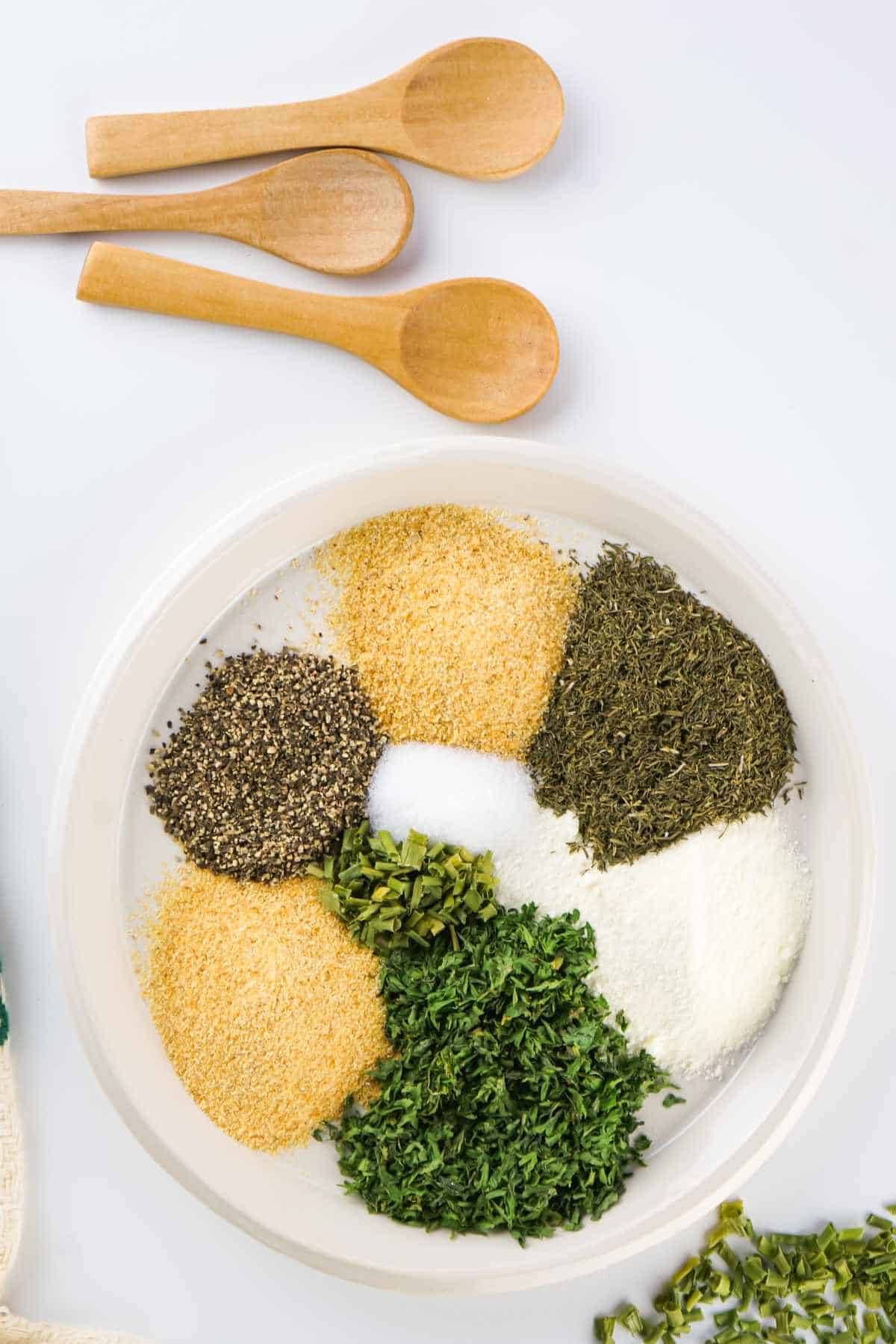 shallow bowl filled with small piles of colorful green, yellow, and white dried herbs, spices, and ingredients.