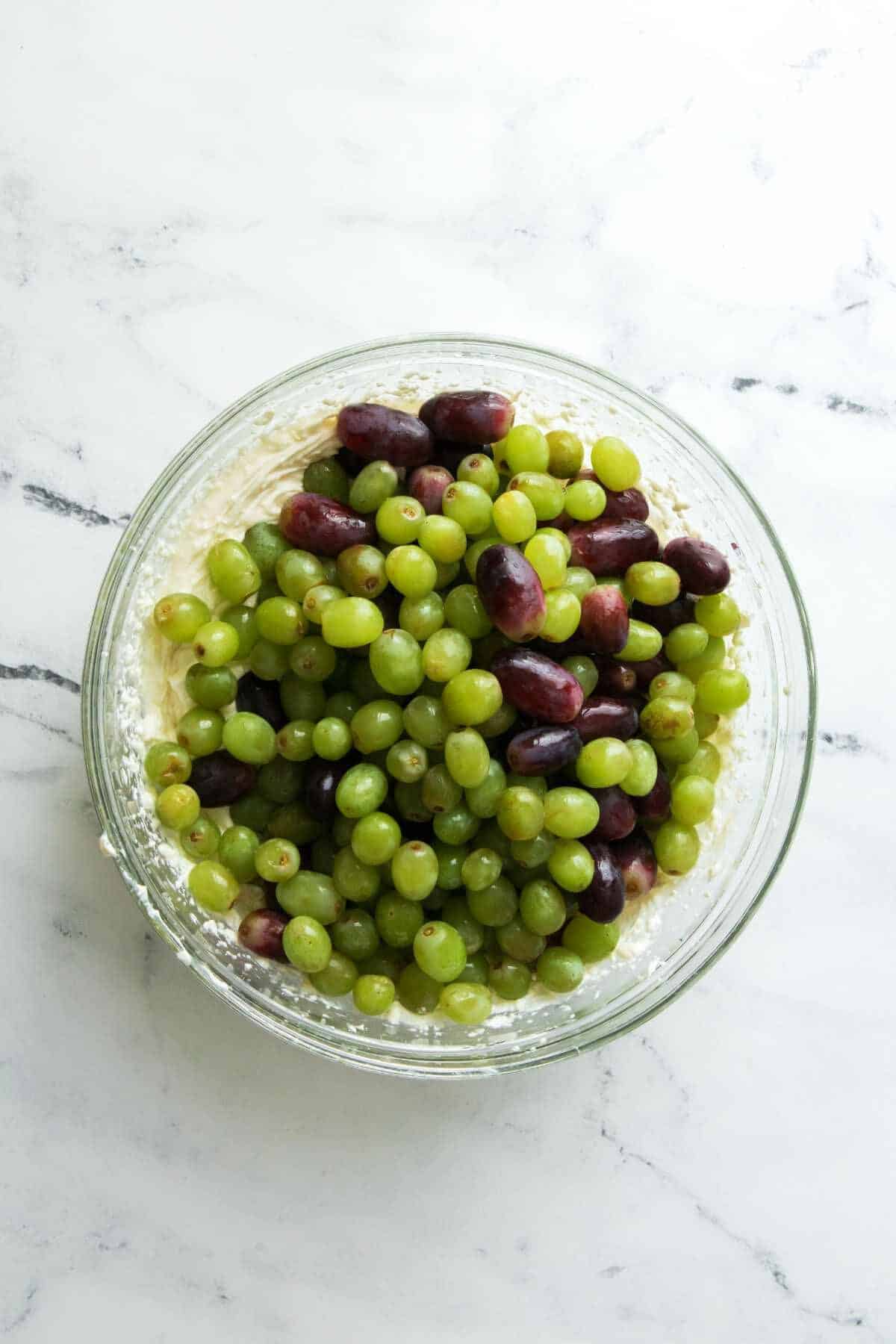 green and red grapes added to a bowl of whipped cream cheese.