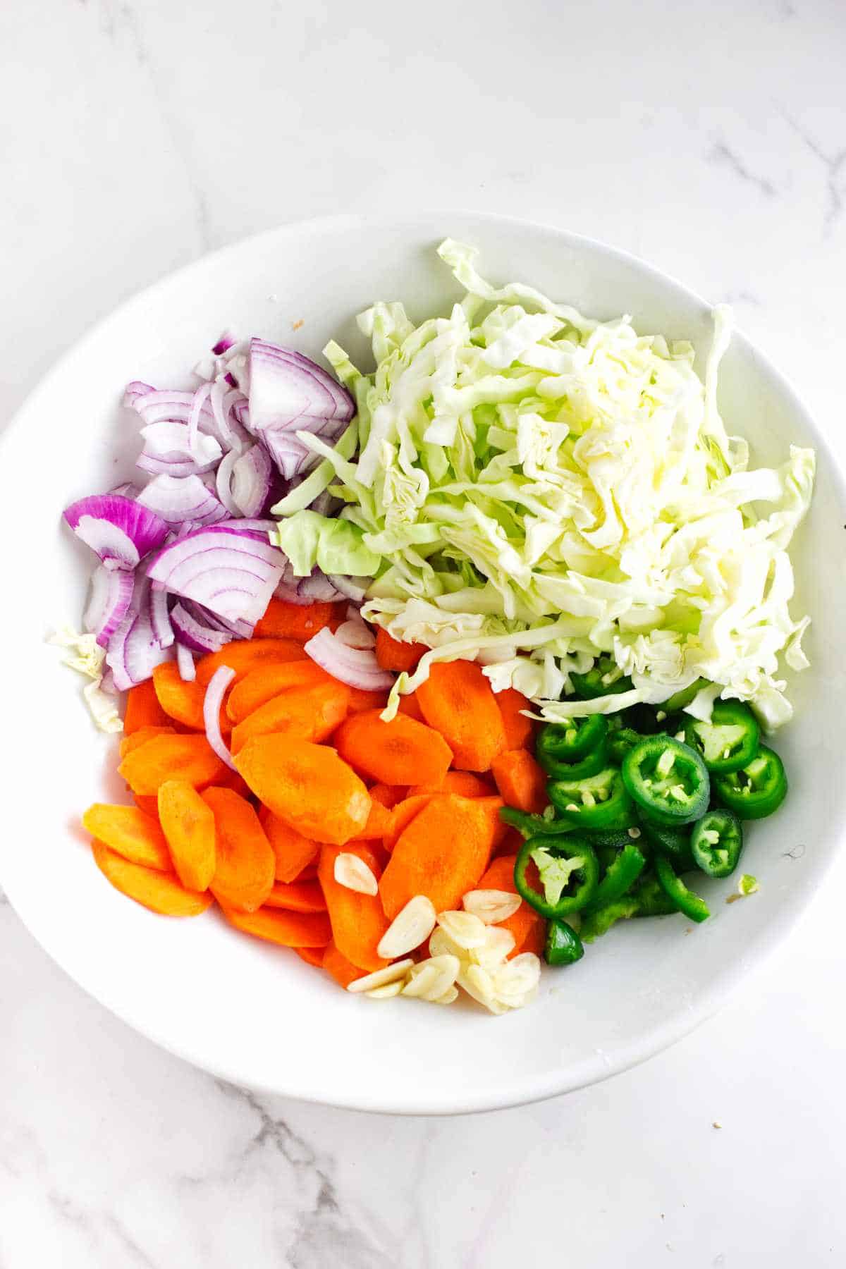 shredded cabbage, diagonally sliced carrots, jalapeno coins, quarter sliced onions and slivered garlic in a large shallow bowl.