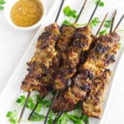 platter of grilled Thai pork skewers (moo ping) with cilantro garnish and spicy peanut dipping sauce.