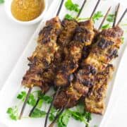 platter of grilled Thai pork skewers (moo ping) with cilantro garnish and spicy peanut dipping sauce.