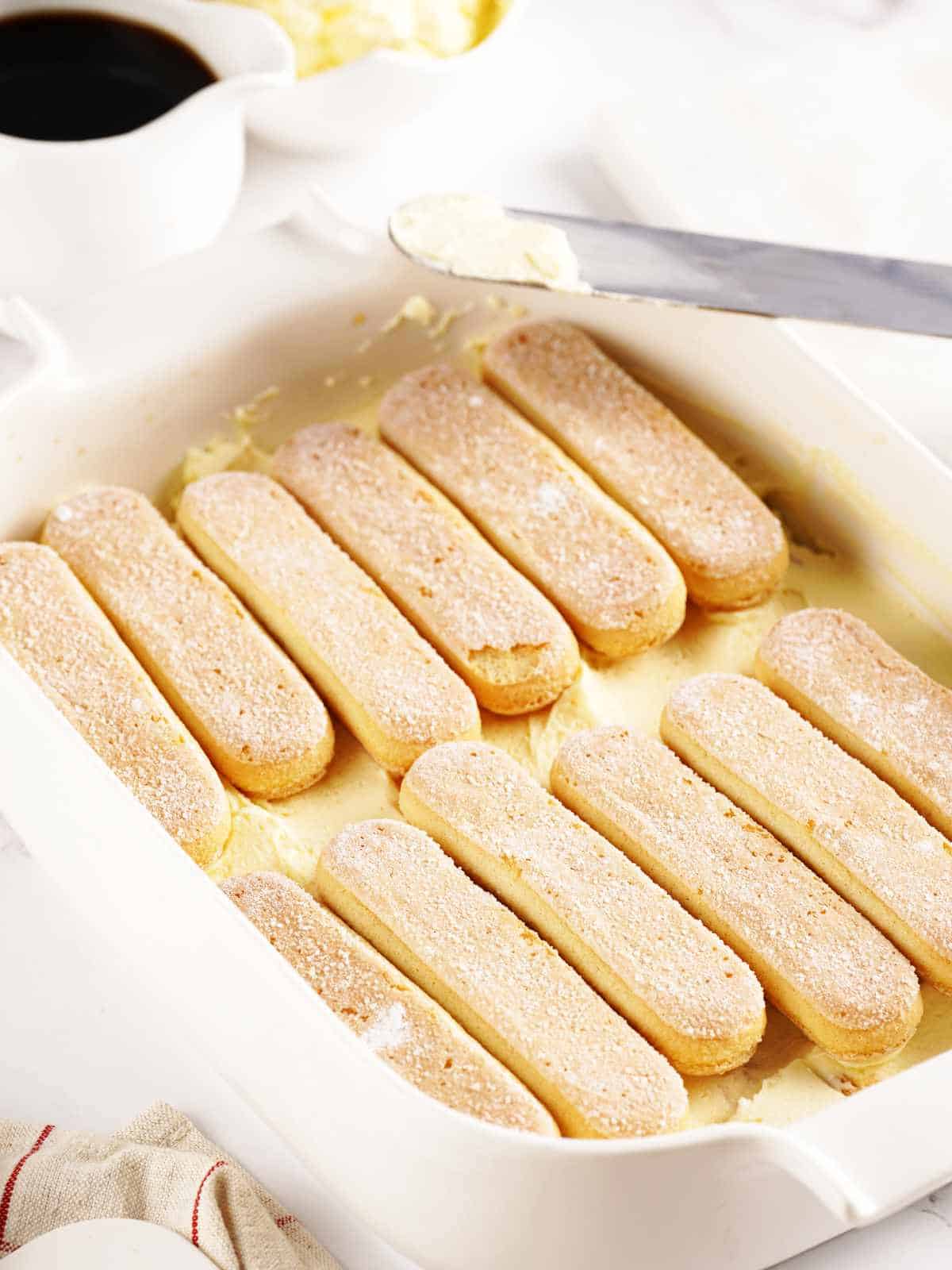 ladyfinger cookies on the bottom of a baking dish on top of layer of custard.