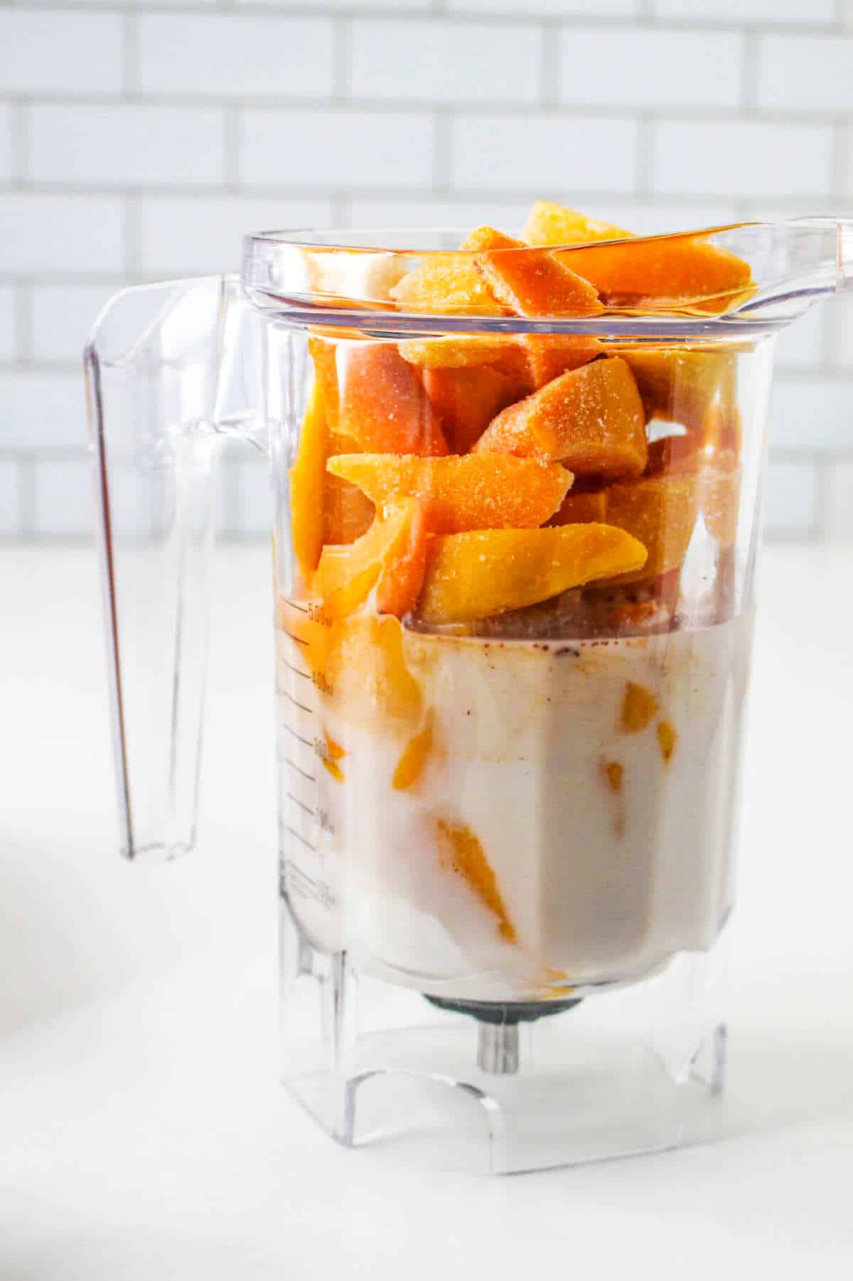 frozen peaches added to a blender with some milk.