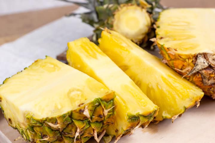 fresh pineapple being cut on counter top.