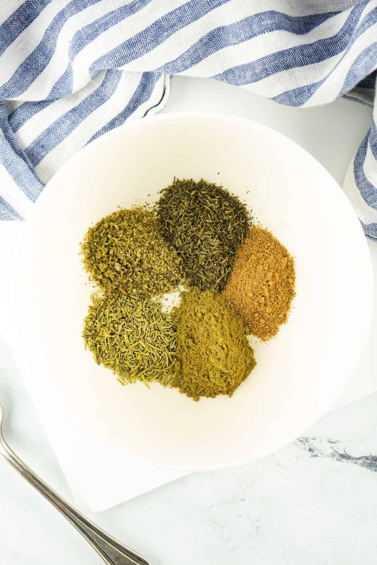 green herbs and spices in a mixing bowl on a white background.
