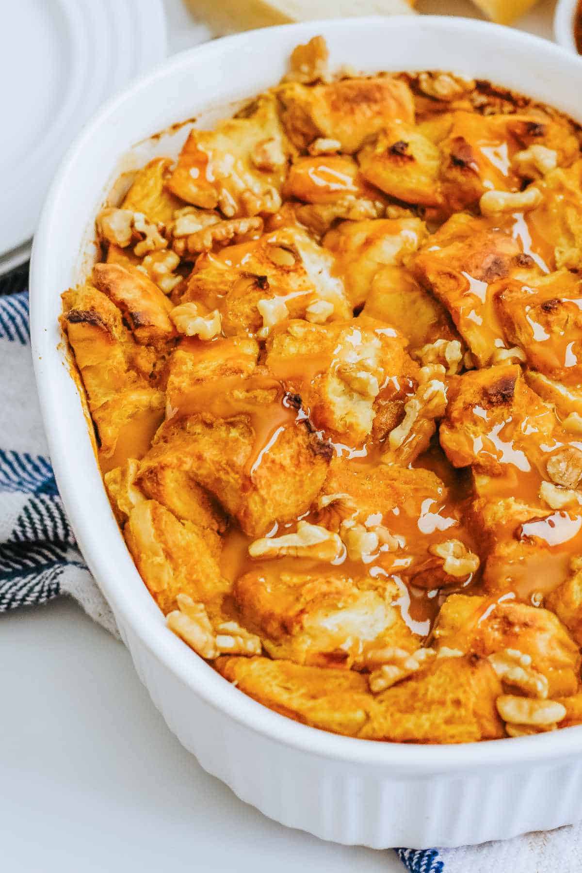 baked bread pudding with nuts scattered on top in an oval white deep dish casserole.