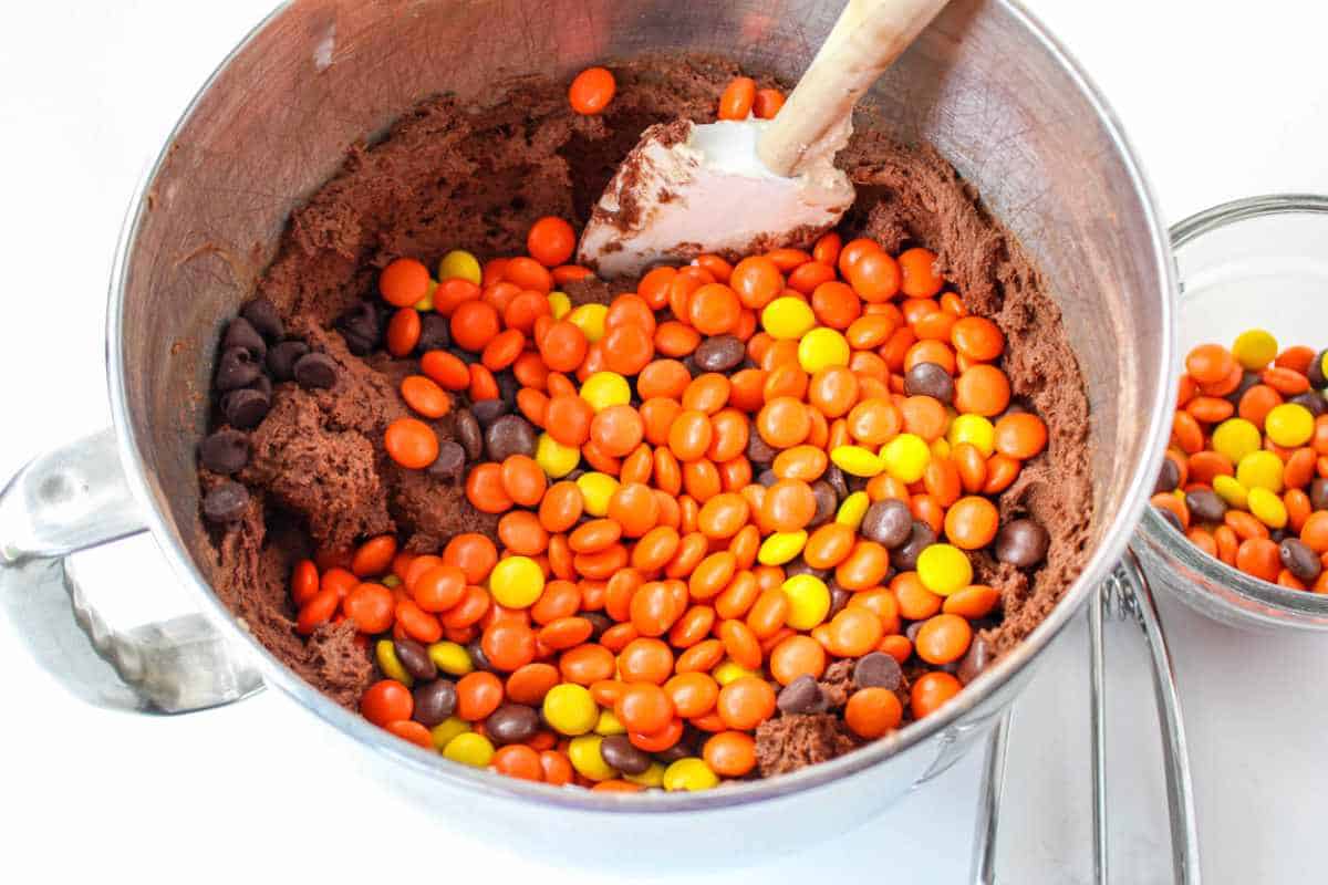 reese's pieces added to cookie batter in a mixing bowl.