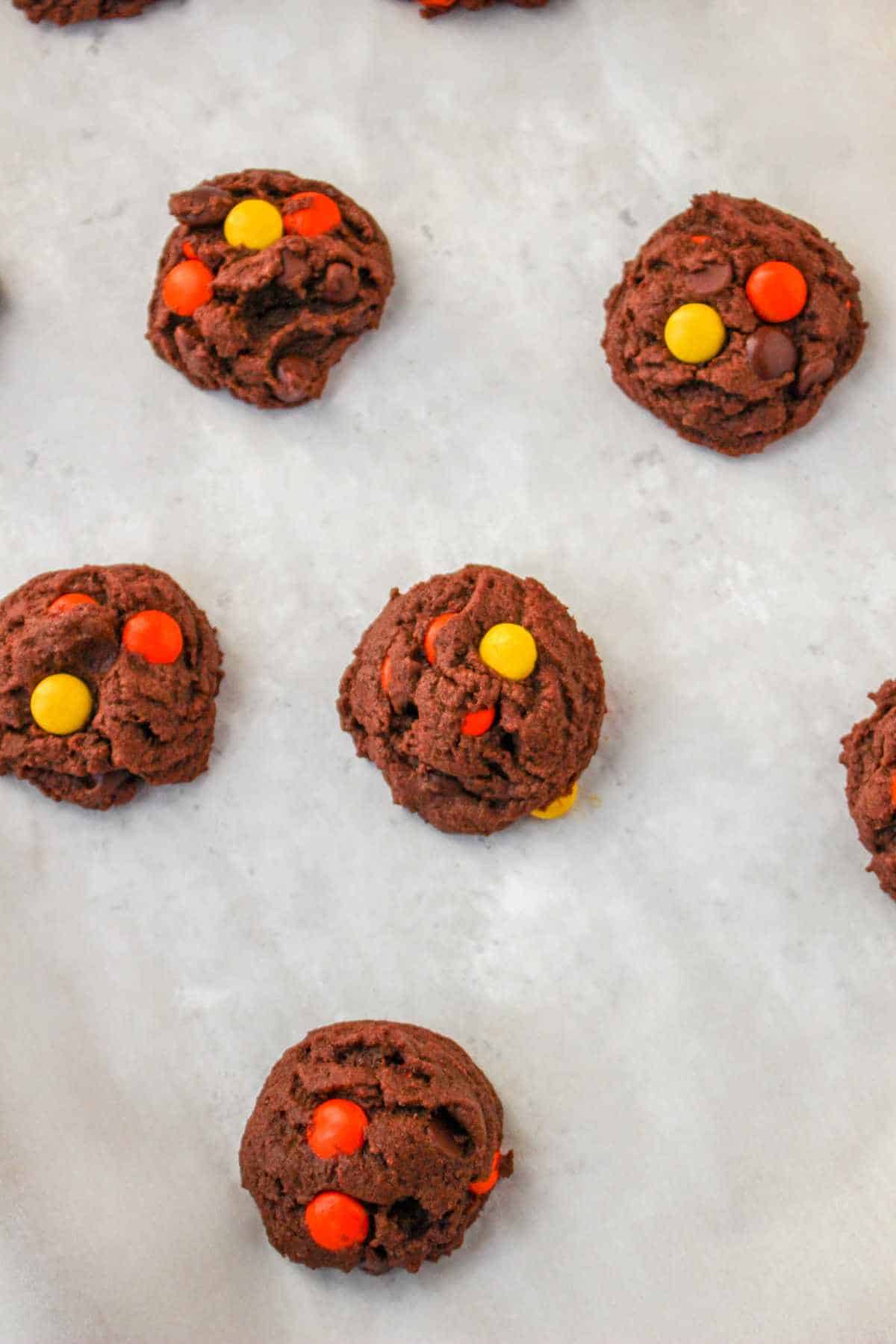 cookie dough scoops on parchment with Reese's pieces studded on top of each cookie.