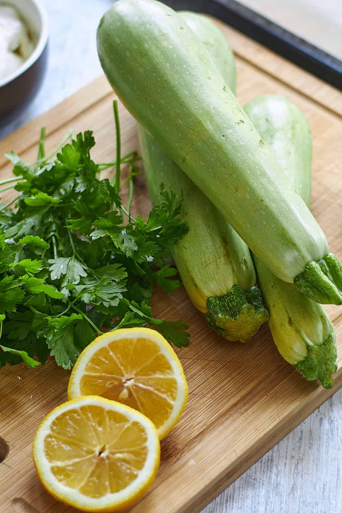 wooden cutting board with zucchini, parsley, and sliced lemon.