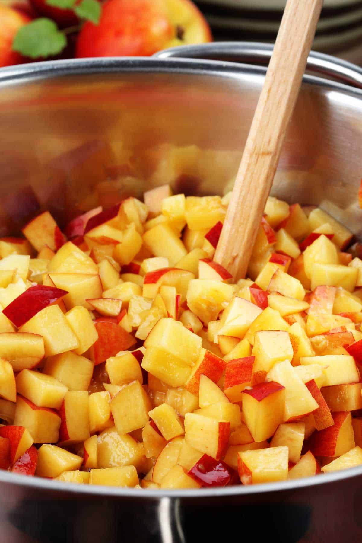 stock pot full of diced peaches and a wooden spoon to stir.