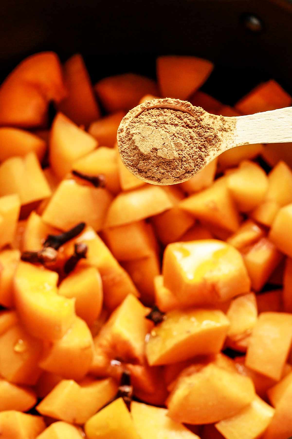 adding cinnamon, vanilla bean caviar, and cloves to pot of cooking diced peaches.