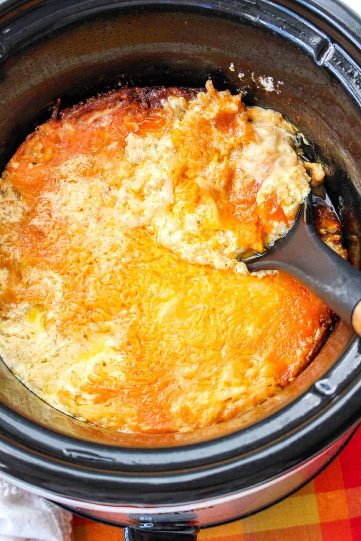 crockpot with scoop of hashbrown casserole in a spoon.