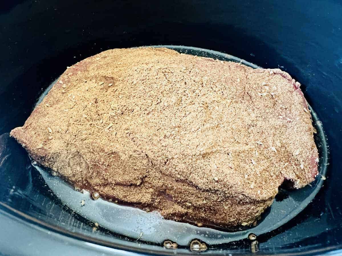 seasoned beef in bottom of a slow cooker.