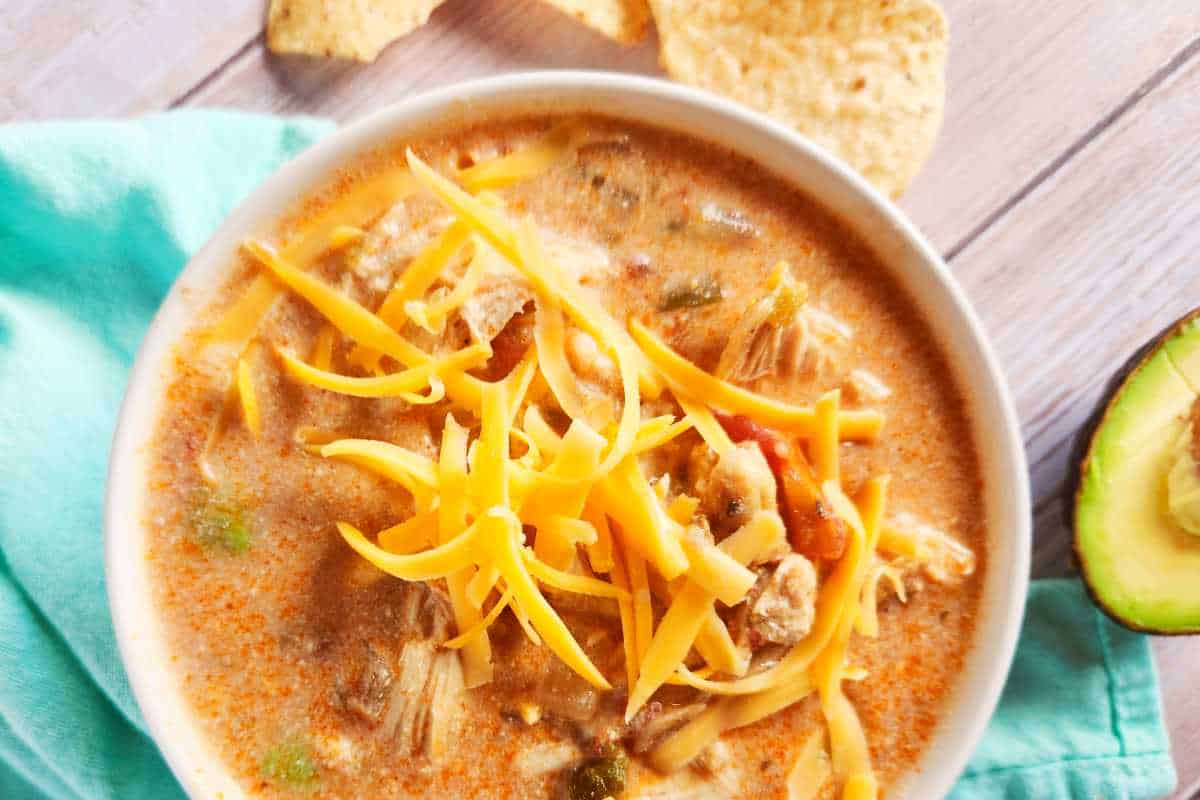 Southwest chicken tortilla soup with shredded cheese and tortilla strips in a bowl.