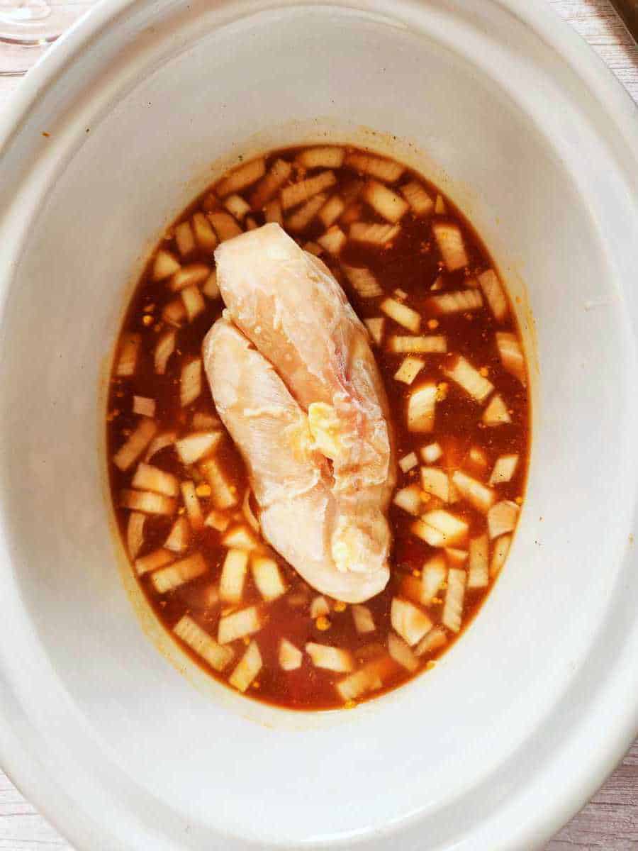 chicken added to crockpot with onions and sauce.