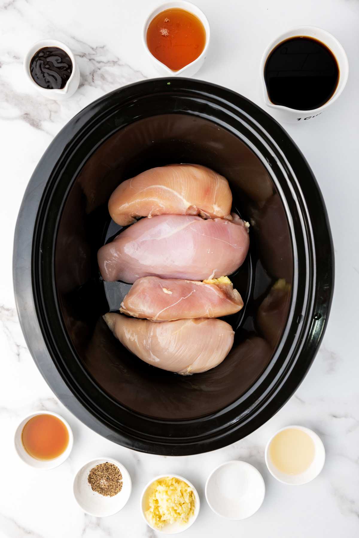 chicken in a slow cooker with bowls of ingredients nearby.