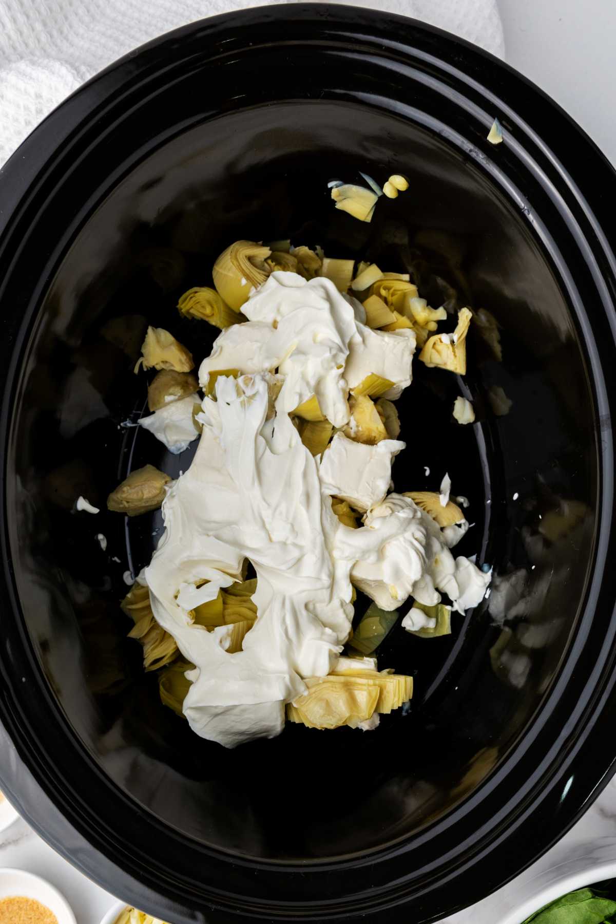 sour cream added on top of cream cheese and vegetable in a crockpot.