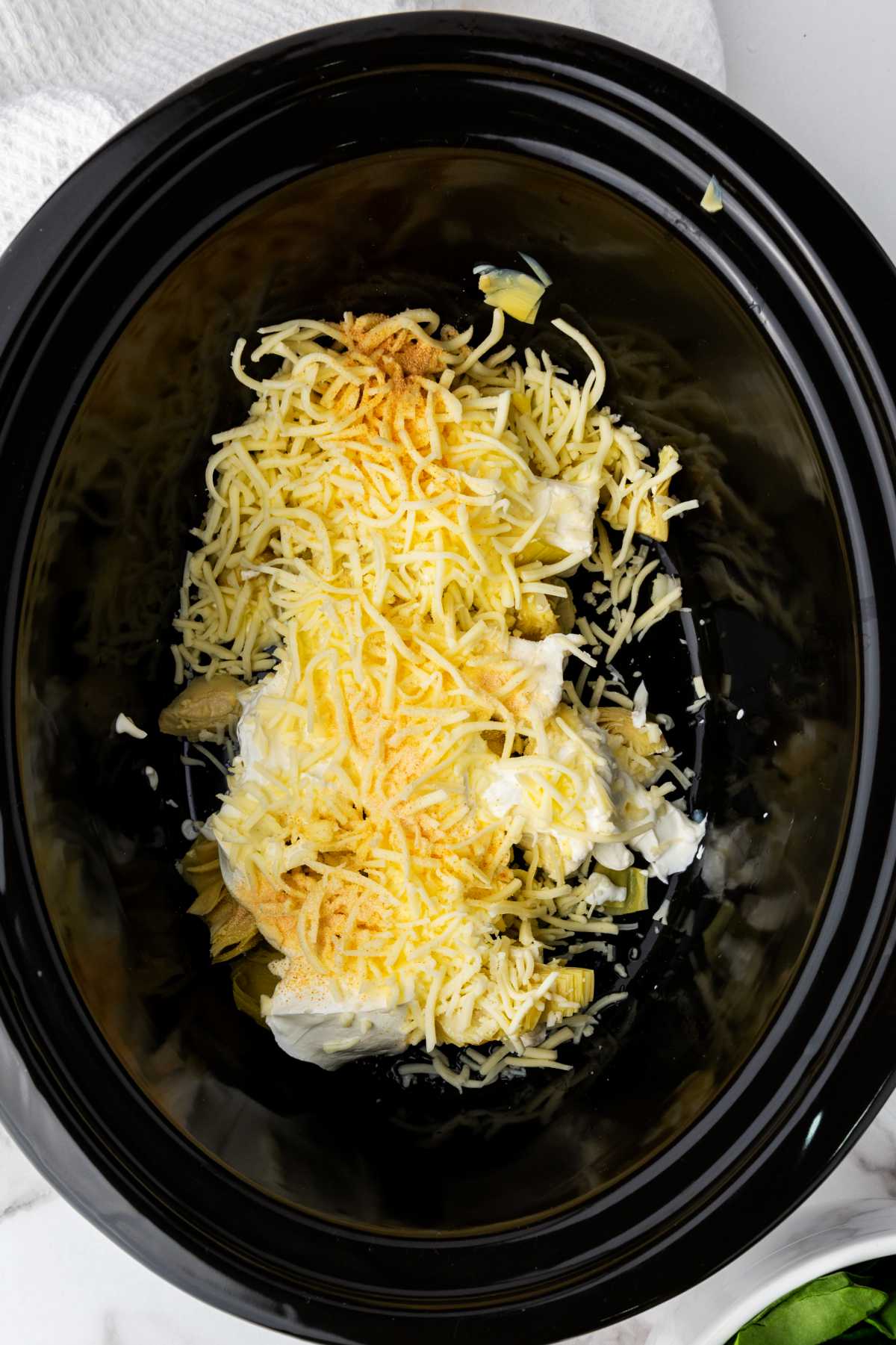 shredded cheese and seasonings added to cream cheese in a crockpot.