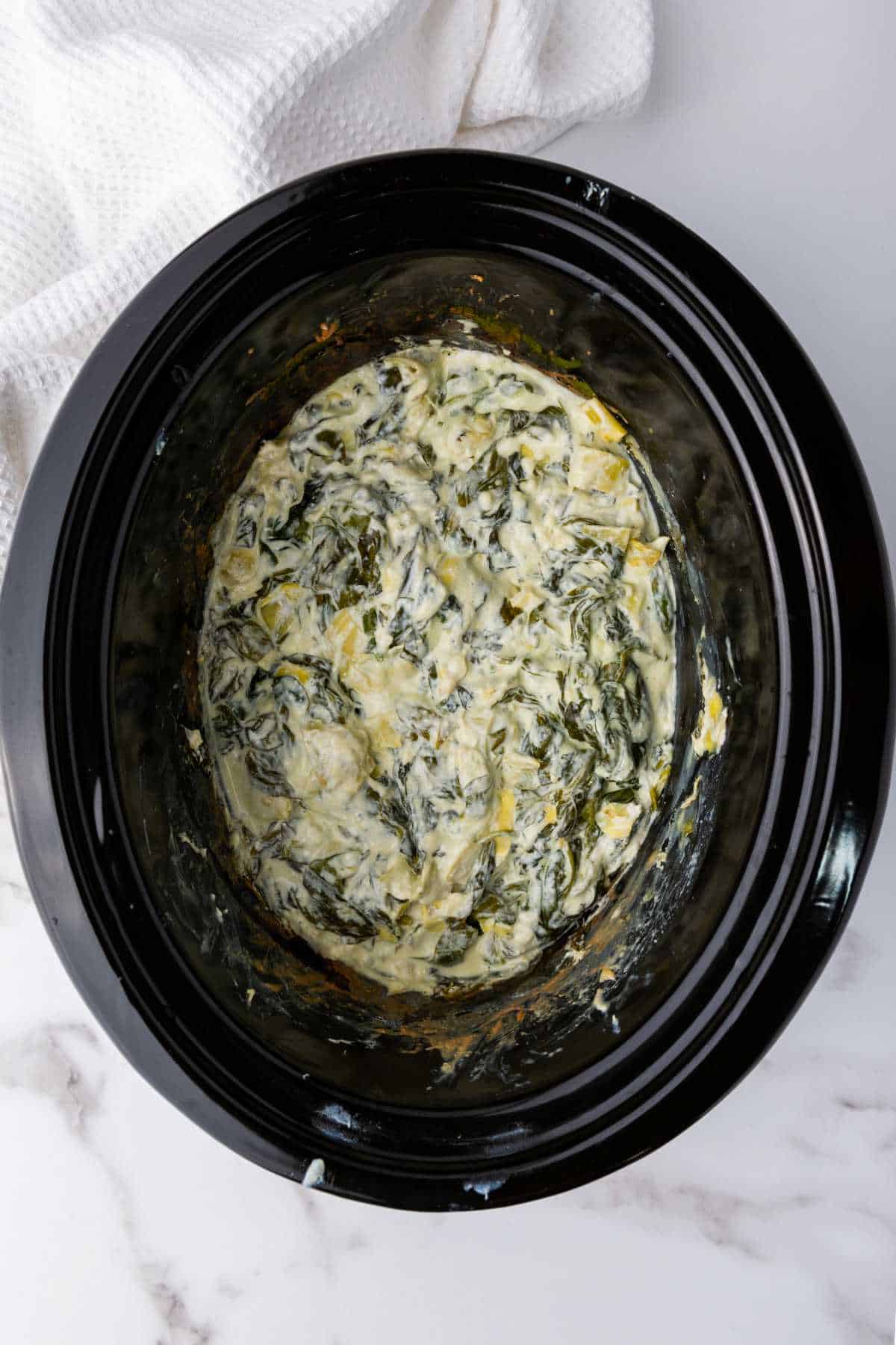 slow cooker with cooked keto spinach artichoke dip.