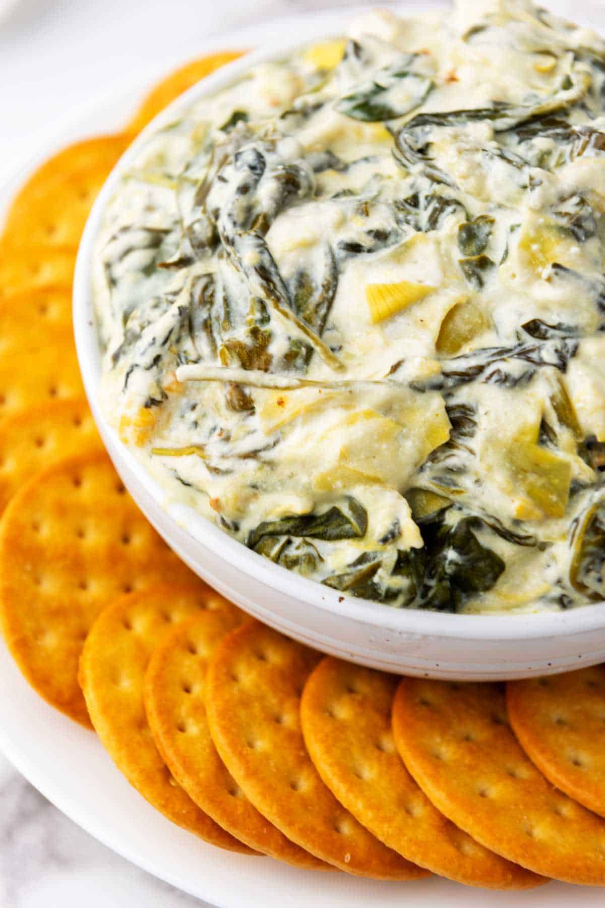 keto spinach artichoke dip in a bowl surrounded by crackers.