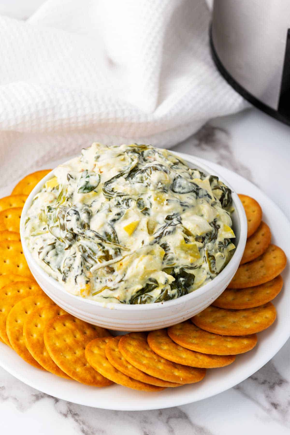 keto spinach artichoke dip in a bowl surrounded by crackers. Perfect for Crocktober.