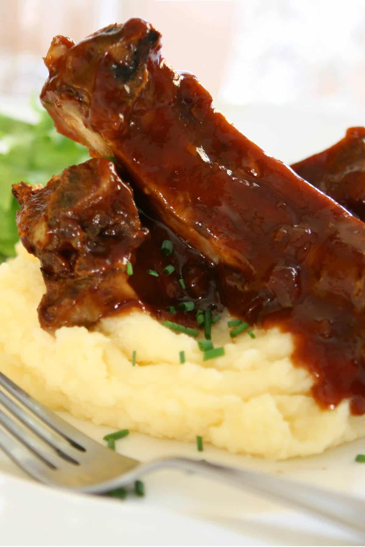 slow cooked beef back ribs on top of mashed potatoes on a plate.
