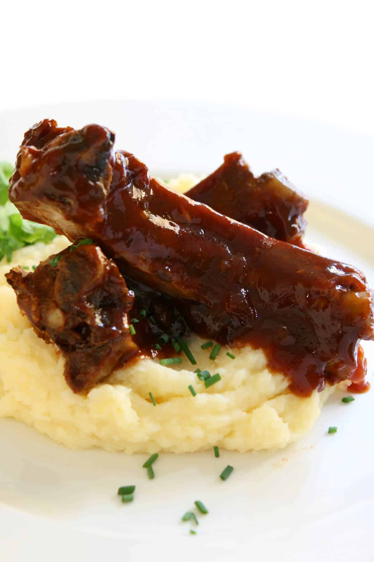 slow cooked beef back ribs on top of mashed potatoes on a plate.