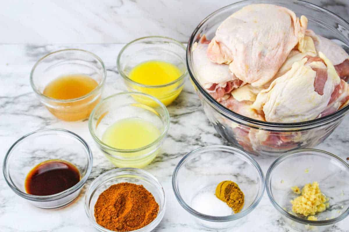 raw chicken, bowls of spices, and seasonings on a white background.