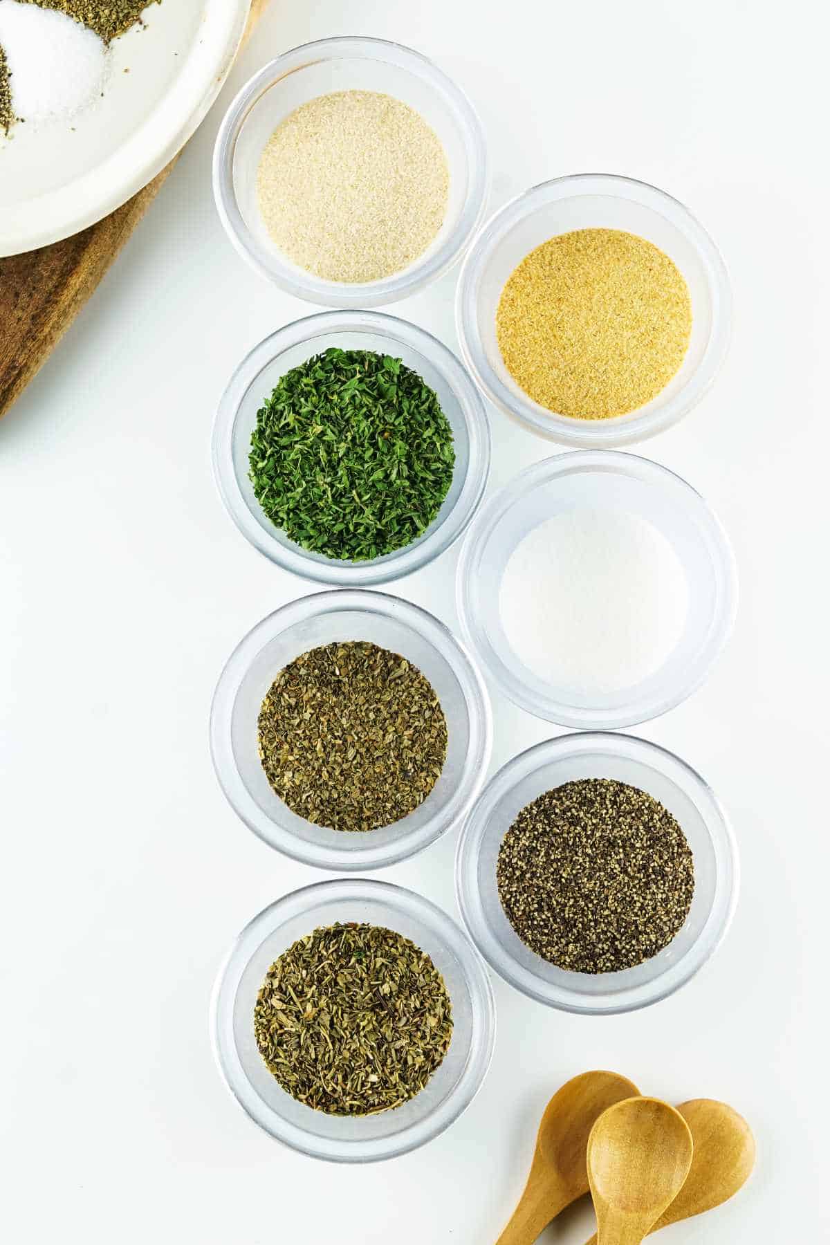 dried herbs and ground spices measured in small bowls for mixing a spice blend.